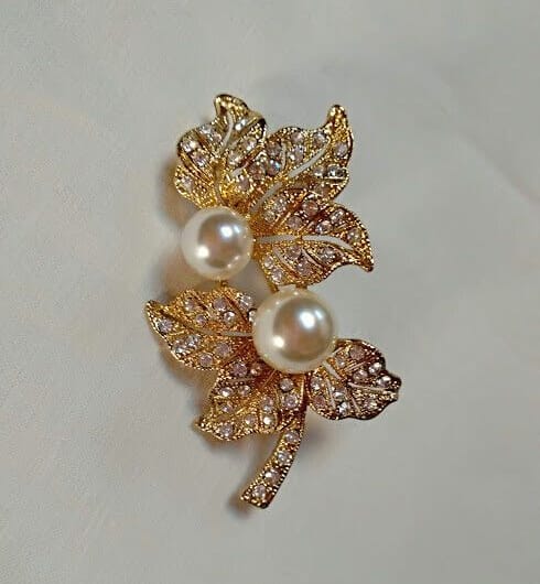 Broche bisuteria dorado con forma de hojas similes blancos y perlas.Nuevo
